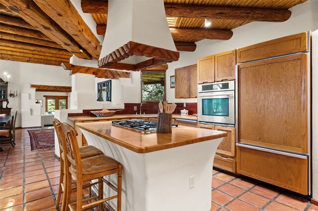 17 Tano W, Santa Fe, NM 87506 - kitchen featuring stainless steel appliances, wooden ceiling with exposed beams, light tile patterned floors, a center island, and a kitchen bar