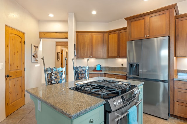 2 Tierra Grande, Santa Fe, NM 87506 - kitchen with stainless steel appliances, a kitchen island, light tile patterned flooring, light stone countertops, and brown cabinetry