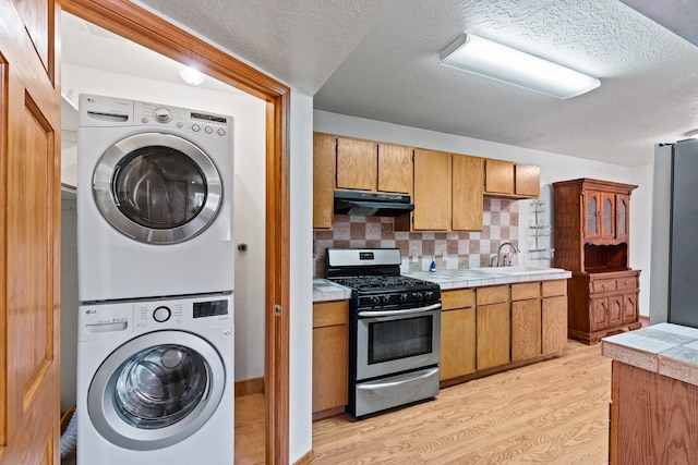 1024 Camino Vista Aurora, Santa Fe, NM 87507 - kitchen featuring appliances with stainless steel finishes, under cabinet range hood, stacked washing machine and dryer, light wood-style floors, and a sink