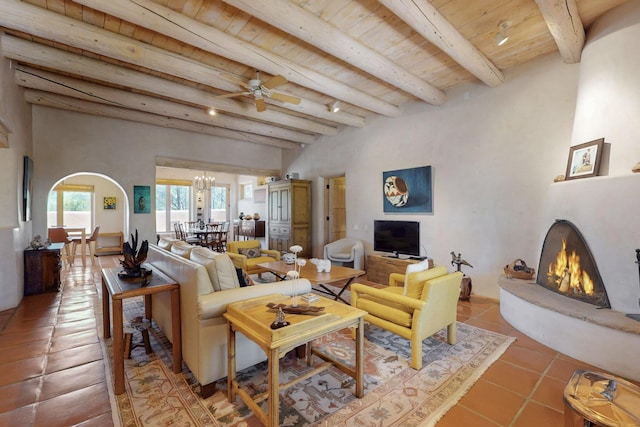 425 Calle Kokopelli, Santa Fe, NM 87501 - tiled living area featuring a warm lit fireplace, wooden ceiling with exposed beams, arched walkways, and a ceiling fan