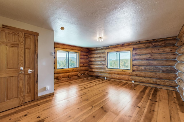 76 Los Altos De Cicuye, Pecos, NM 87552 - spare room featuring plenty of natural light, wood-type flooring, a textured ceiling, log walls, and baseboards