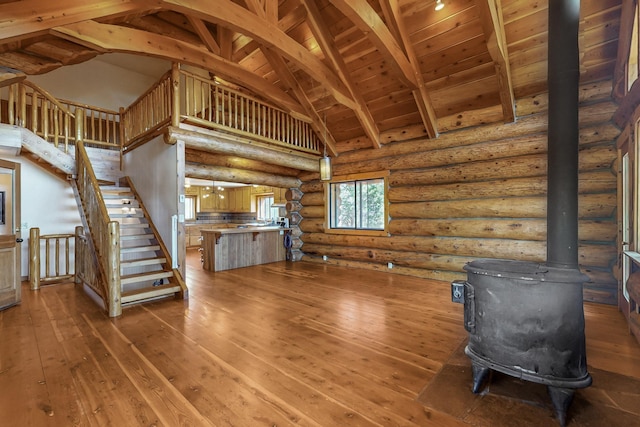 76 Los Altos De Cicuye, Pecos, NM 87552 - unfurnished living room featuring a wood stove, hardwood / wood-style flooring, high vaulted ceiling, rustic walls, and stairs