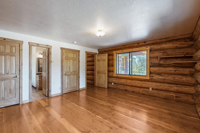 76 Los Altos De Cicuye, Pecos, NM 87552 - unfurnished bedroom featuring hardwood / wood-style flooring, a textured ceiling, baseboards, connected bathroom, and log walls