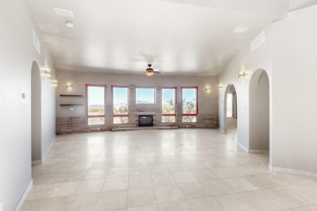 5 La Aguapa, Sandia Park, NM 87047 - unfurnished living room featuring a ceiling fan, arched walkways, a glass covered fireplace, baseboards, and light tile patterned floors