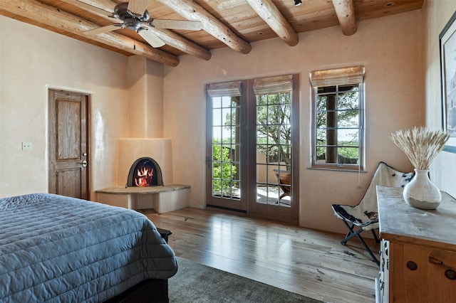 1050 Sierra Del Norte, Santa Fe, NM 87501 - bedroom featuring wood ceiling with exposed beams, access to outside, hardwood / wood-style flooring, and a warm lit fireplace