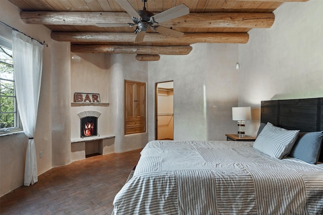 1050 Sierra Del Norte, Santa Fe, NM 87501 - bedroom with wood ceiling with exposed beams, brick flooring, and a warm lit fireplace