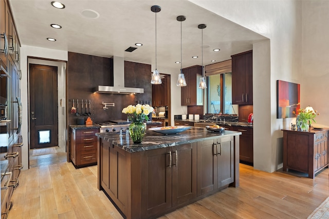 20 Rising Moon, Santa Fe, NM 87506 - kitchen featuring wall chimney exhaust hood, light wood finished floors, dark stone counters, a kitchen island, and recessed lighting