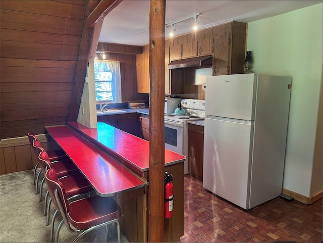 7 W Meadow Ln, Sapello, NM 87745 - kitchen with white appliances, under cabinet range hood, wooden walls, track lighting, and brown cabinets
