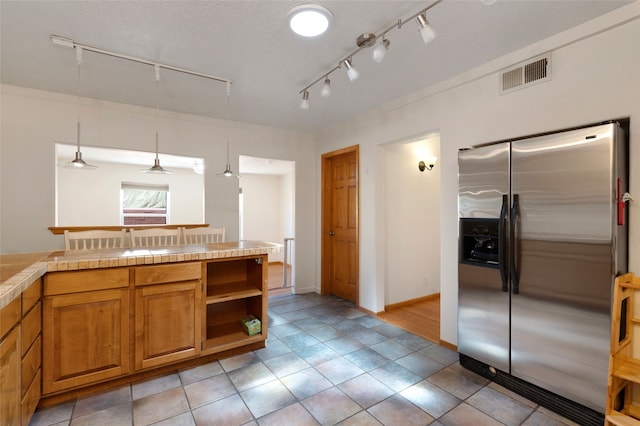 1208 Declovina St, Santa Fe, NM 87505 - kitchen with stainless steel fridge with ice dispenser, rail lighting, brown cabinets, decorative light fixtures, and light tile patterned floors