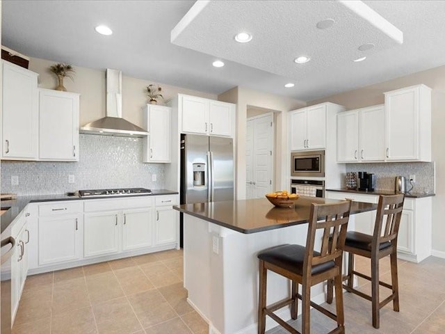 5220 Gold Hill Ln, Santa Fe, NM 87507 - kitchen featuring wall chimney exhaust hood, appliances with stainless steel finishes, dark countertops, a kitchen bar, and backsplash