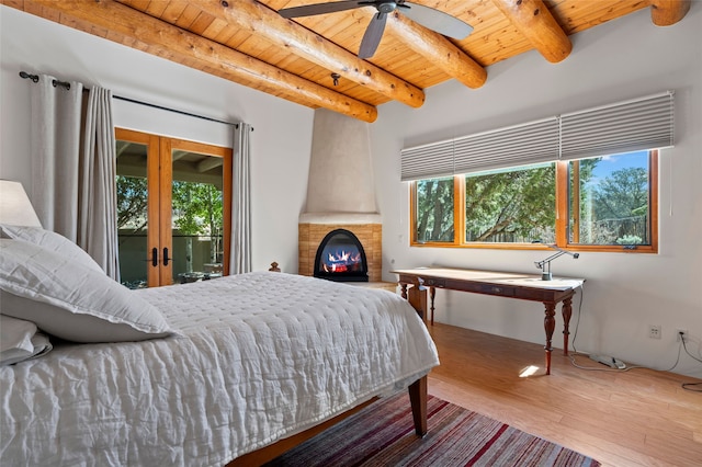 557 Valle Chamiso Ln, Santa Fe, NM 87505 - bedroom featuring wood ceiling with exposed beams, wood finished floors, access to exterior, and a large fireplace