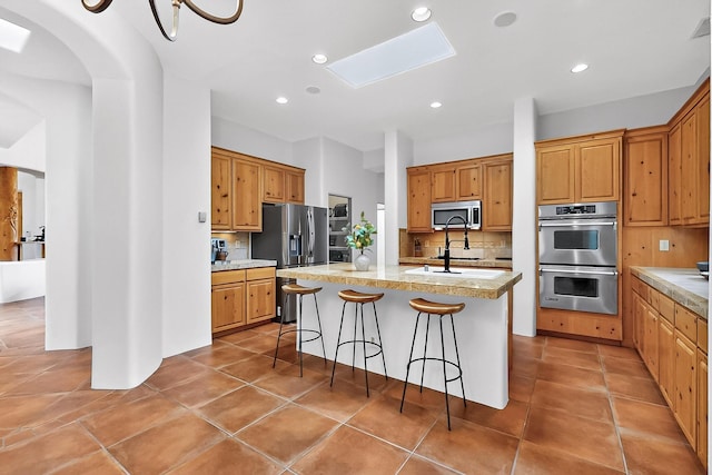 138 E Chili Line, Santa Fe, NM 87508 - kitchen featuring stainless steel appliances, decorative backsplash, a kitchen island with sink, a skylight, and a breakfast bar area