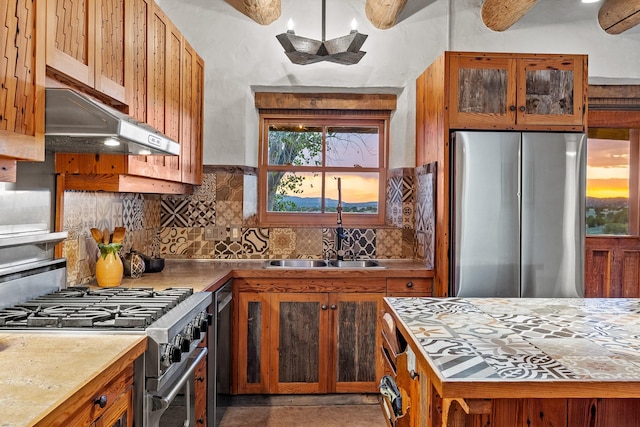 26 Camino Los Angelitos, Santa Fe, NM 87540 - kitchen with appliances with stainless steel finishes, under cabinet range hood, a sink, brown cabinetry, and tasteful backsplash
