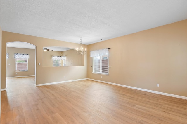 2613 Camino Catalonia, Rio Rancho, NM 87124 - unfurnished room with a chandelier, light wood finished floors, arched walkways, baseboards, and a textured ceiling