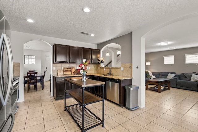 6280 Nardos Rd NW, Albuquerque, NM 87114 - kitchen with arched walkways, appliances with stainless steel finishes, dark brown cabinets, a sink, and a textured ceiling