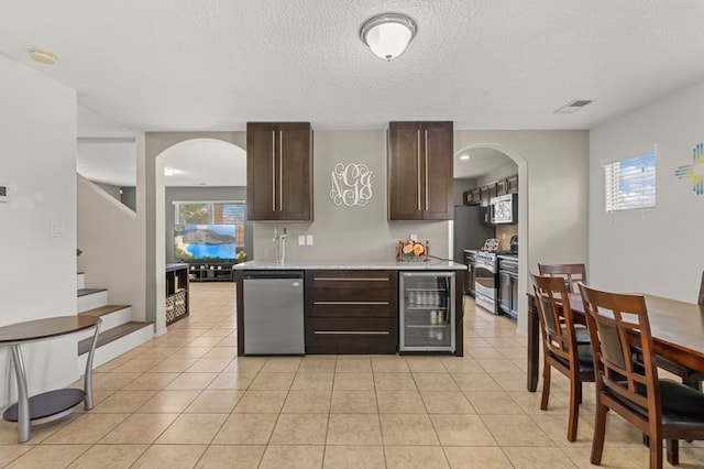6280 Nardos Rd NW, Albuquerque, NM 87114 - kitchen with appliances with stainless steel finishes, beverage cooler, arched walkways, dark brown cabinetry, and healthy amount of natural light