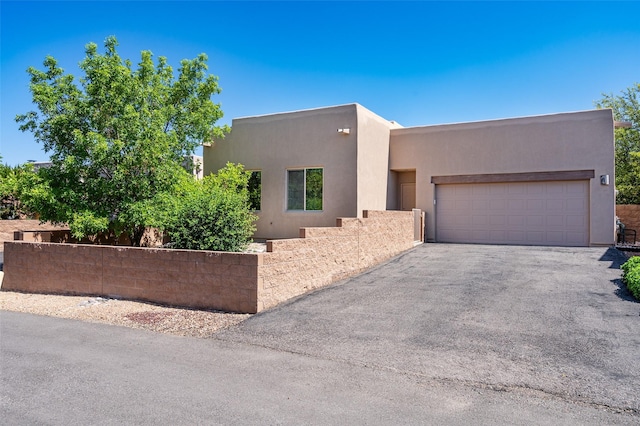 15 Cimarron Pass, Santa Fe, NM 87508 - pueblo-style house with stucco siding, asphalt driveway, and an attached garage