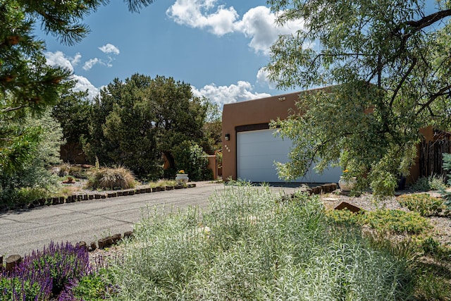 678 Callecita Jicarilla, Santa Fe, NM 87505 - view of side of home featuring concrete driveway, stucco siding, an attached garage, and an outbuilding