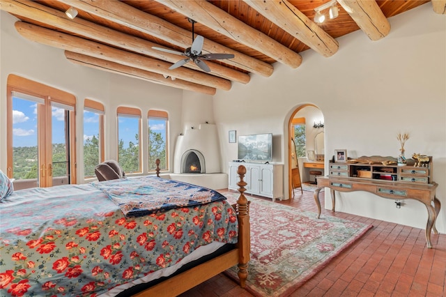17 Alteza, Santa Fe, NM 87508 - bedroom featuring a wood ceiling with exposed beams, arched walkways, brick flooring, a lit fireplace, and ensuite bath