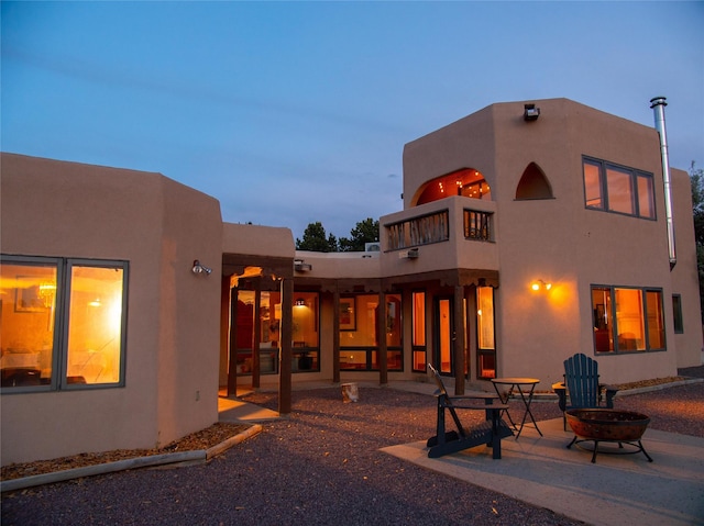 7 Paseo De Rincon, Santa Fe, NM 87508 - back of property at dusk featuring a fire pit, a balcony, a patio, and stucco siding