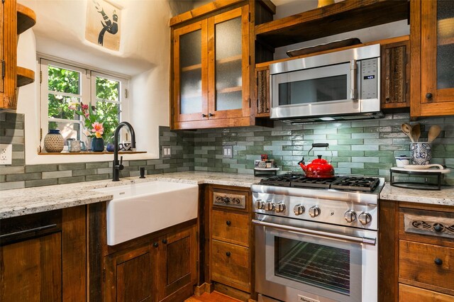 576 Camino Del Monte Sol, Santa Fe, NM 87505 - kitchen featuring stainless steel appliances, decorative backsplash, light stone counters, and glass insert cabinets