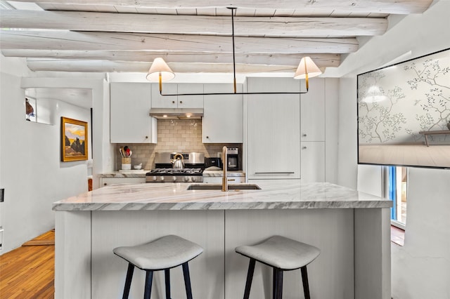 507 Acequia Madre, Santa Fe, NM 87505 - kitchen with stainless steel gas stove, under cabinet range hood, backsplash, a kitchen bar, and beam ceiling