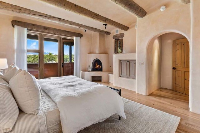 16 Plazuela Intimo, Santa Fe, NM 87506 - bedroom featuring arched walkways, light wood-style flooring, beam ceiling, and a lit fireplace