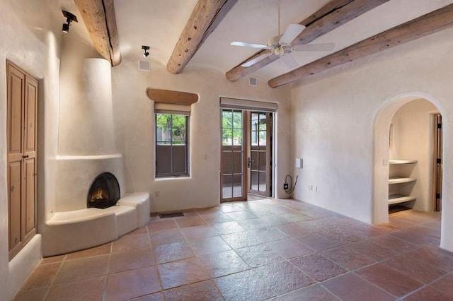 16 Plazuela Intimo, Santa Fe, NM 87506 - unfurnished living room with stone tile floors, beamed ceiling, a ceiling fan, and arched walkways