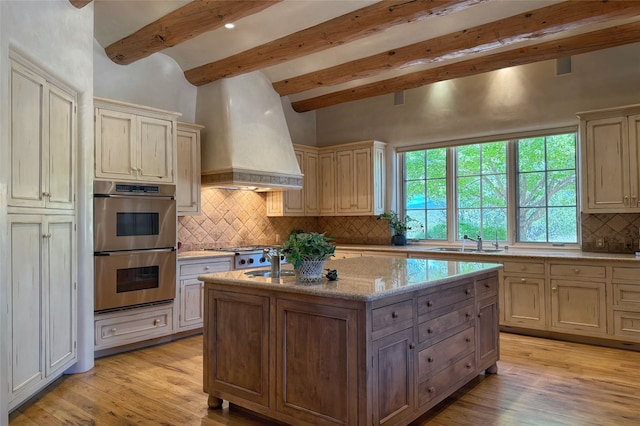 11 E Golden Eagle Rd, Santa Fe, NM 87506 - kitchen featuring custom exhaust hood, double oven, beamed ceiling, light wood-style floors, and decorative backsplash