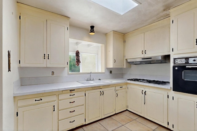 1017 Practilliano Dr, Santa Fe, NM 87505 - kitchen with oven, stainless steel gas stovetop, under cabinet range hood, a skylight, and light tile patterned flooring