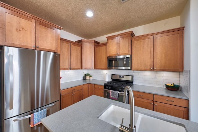 139 Rancho Viejo Blvd, Santa Fe, NM 87508 - kitchen with appliances with stainless steel finishes, a textured ceiling, brown cabinetry, tasteful backsplash, and light countertops