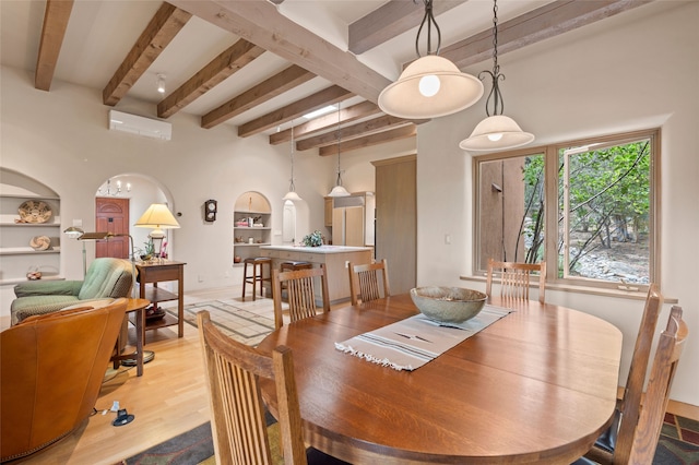 1203 Sierra Del Este, Santa Fe, NM 87501 - dining space featuring beam ceiling, arched walkways, built in shelves, a wall mounted air conditioner, and light wood-type flooring