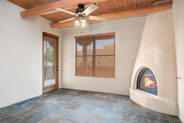 1405 Vegas Verdes Unit 136, Santa Fe, NM 87507 - unfurnished living room featuring a wooden ceiling with exposed beams, stone tile flooring, ceiling fan, and a large fireplace