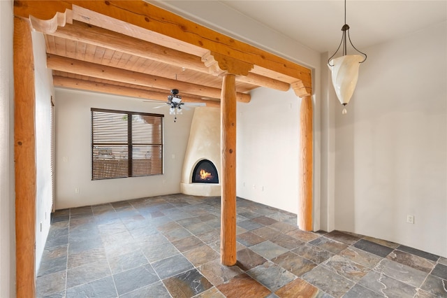 1405 Vegas Verdes Unit 136, Santa Fe, NM 87507 - unfurnished living room featuring stone tile flooring, ceiling fan, beam ceiling, and a large fireplace