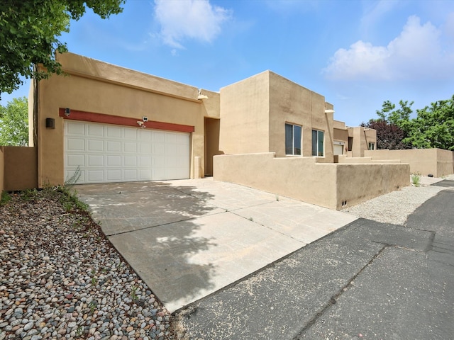 16 Coyote Pass Rd, Santa Fe, NM 87508 - pueblo revival-style home with concrete driveway, stucco siding, and a garage
