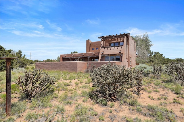 35 Avenida De La Paz, Lamy, NM 87540 - back of house with a pergola, stucco siding, and a chimney