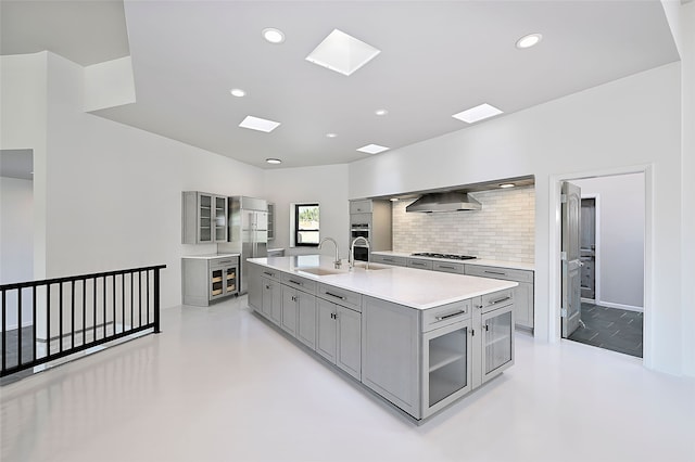 117 La Ventana, Santa Fe, NM 87508 - kitchen with gray cabinetry, wall chimney range hood, light countertops, gas stovetop, and glass insert cabinets