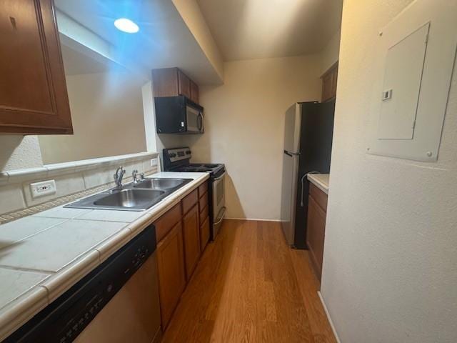 2210 Miguel Chavez Unit 1816, Santa Fe, NM 87505 - kitchen featuring appliances with stainless steel finishes, light wood finished floors, tile countertops, electric panel, and brown cabinetry