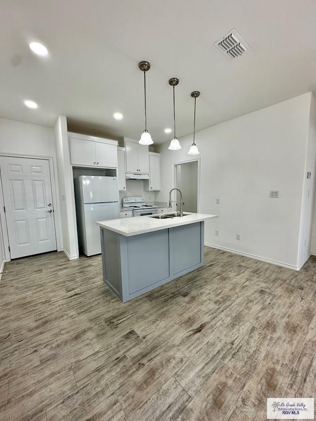 kitchen with white appliances, a kitchen island with sink, sink, hanging light fixtures, and hardwood / wood-style flooring