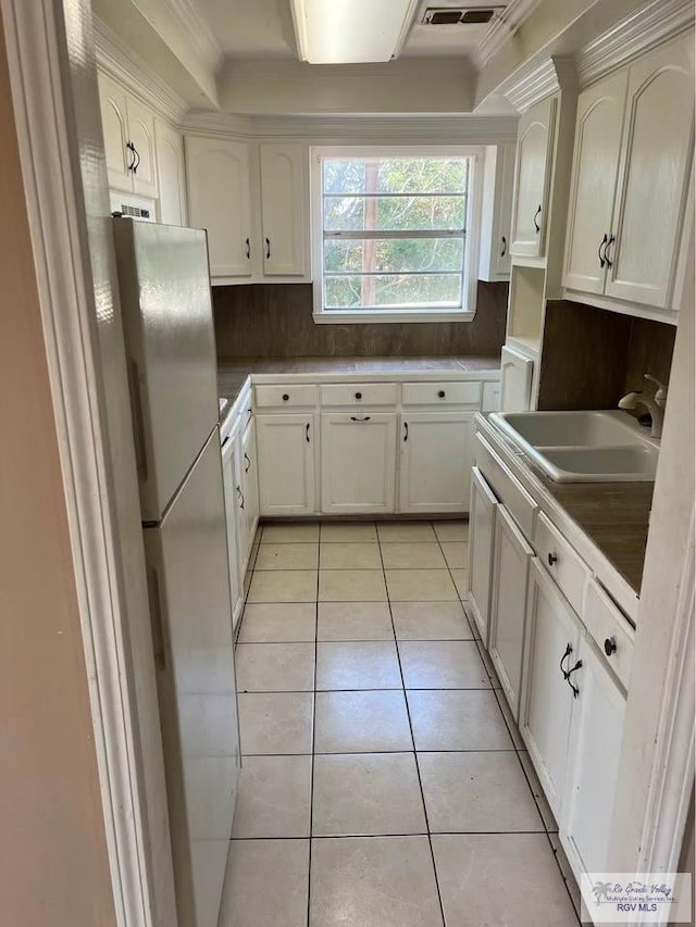 kitchen featuring light tile patterned flooring, white cabinets, freestanding refrigerator, and a sink