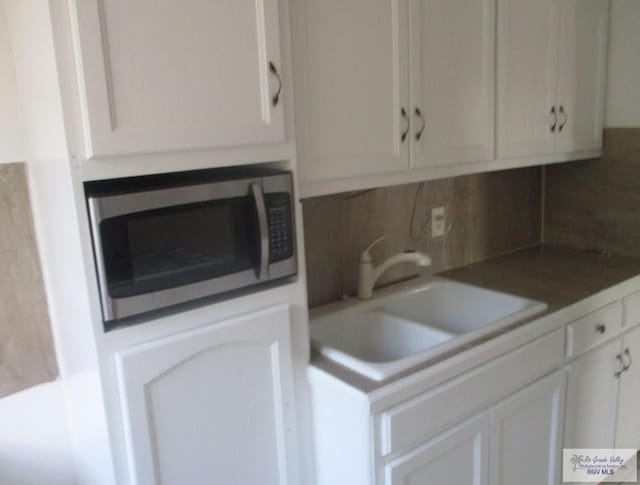 kitchen featuring white cabinetry, stainless steel microwave, backsplash, and a sink