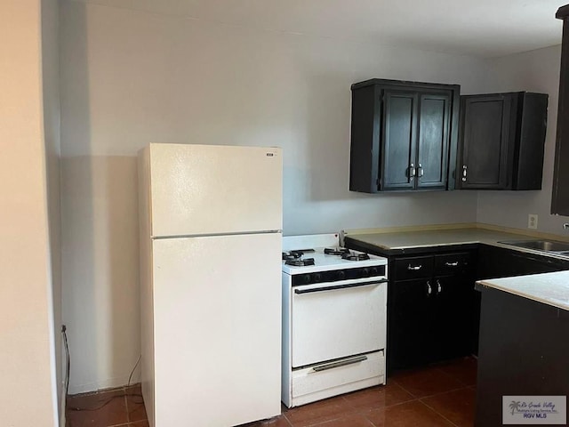 kitchen with dark tile patterned floors, a sink, dark cabinetry, white appliances, and light countertops