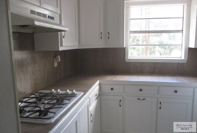 kitchen featuring white cabinets, gas stovetop, tasteful backsplash, and under cabinet range hood