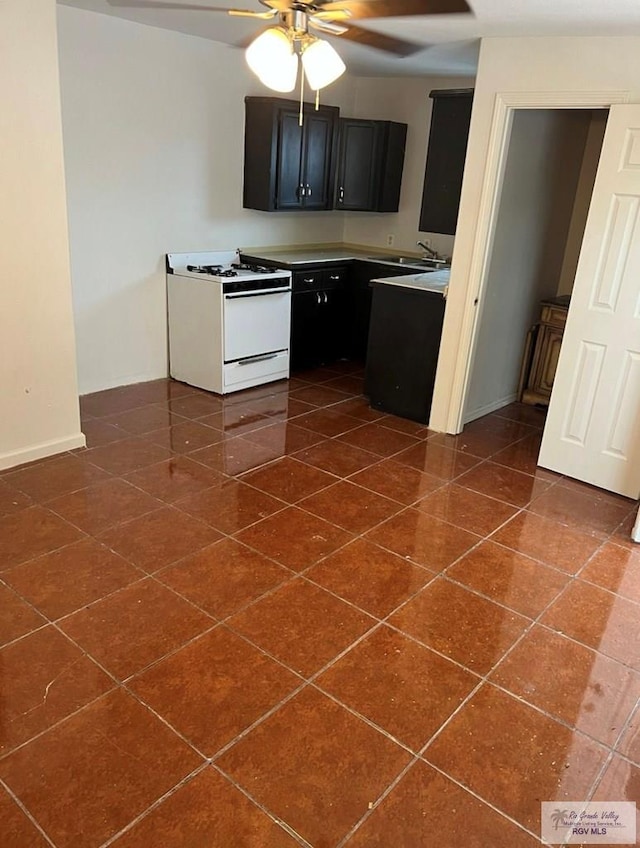 kitchen with baseboards, white gas range oven, dark cabinetry, a ceiling fan, and a sink