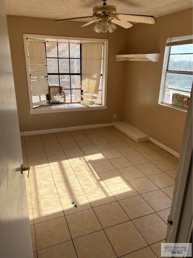 tiled empty room featuring baseboards, a textured ceiling, and a ceiling fan