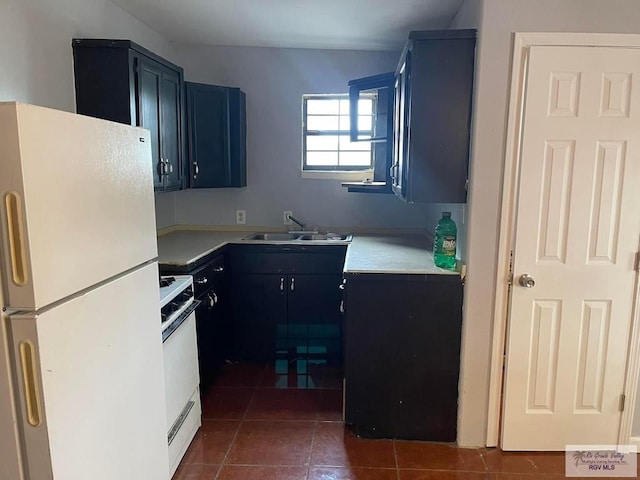 kitchen featuring blue cabinetry, dark tile patterned flooring, light countertops, white appliances, and a sink