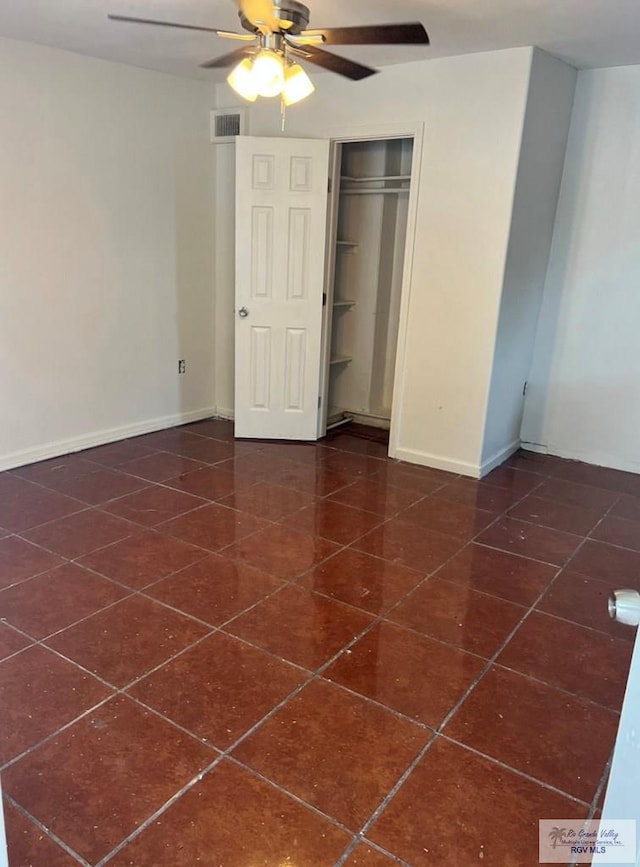 unfurnished bedroom featuring visible vents, dark tile patterned floors, a closet, baseboards, and ceiling fan