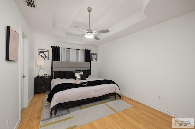 bedroom with baseboards, visible vents, a tray ceiling, and wood finished floors