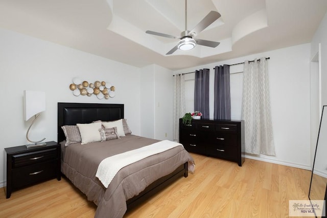 bedroom featuring a tray ceiling, ceiling fan, and light wood finished floors