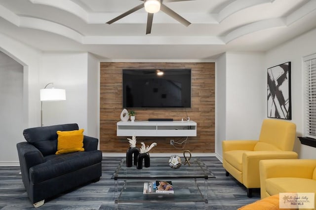 living area featuring an accent wall, a tray ceiling, a ceiling fan, and baseboards